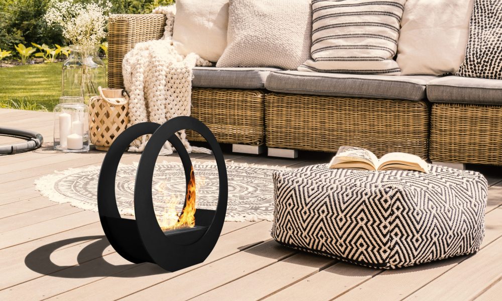 Pouf and rattan sofa on wooden patio with hanging chair in the garden. Real photo
